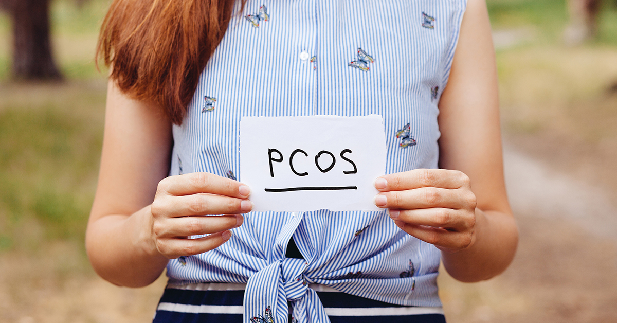 woman holding pcos sign; blog: polycystic ovary syndrome explained