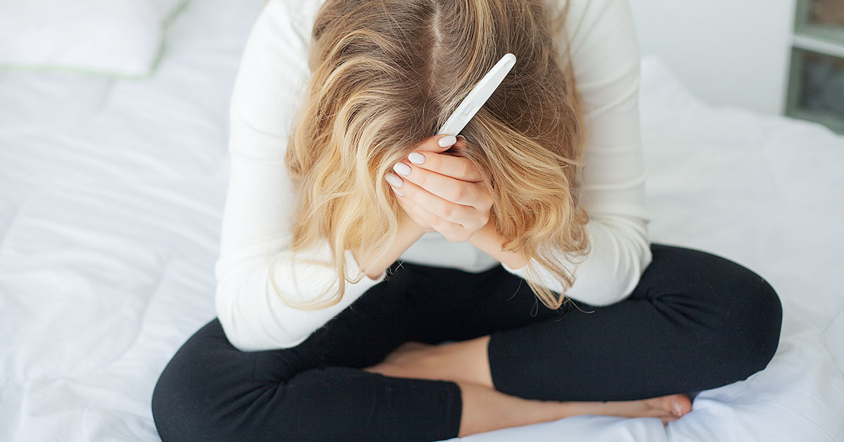 Positive pregnancy test. Young woman feeling depressed and sad after looking at pregnancy test result at home; blog: Taking Care of Yourself While Dealing with Infertility