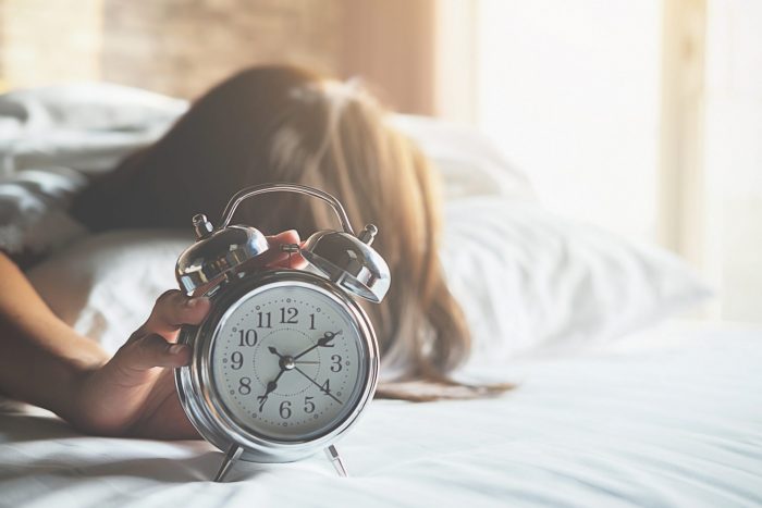 Age and Fertility: The Truth; Irritated young woman putting her alarm clock off in the morning with soft morning light. Relaxing concept. About Your Biological Clock