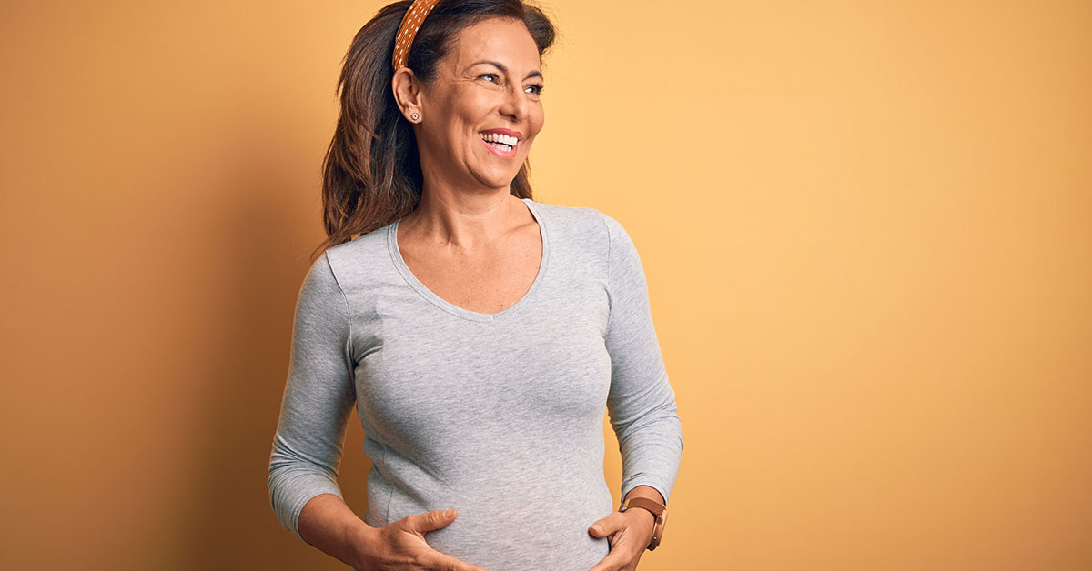 Middle age pregnant woman expecting baby at aged pregnancy looking away to side with smile on face, natural expression. Laughing confident; blog: What is Advanced Maternal Age?