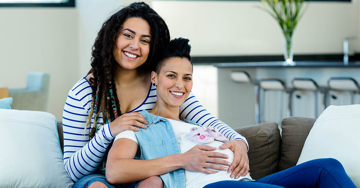 Pregnant lesbian couple with a pair of pink baby shoes; blog: Fertility Options for Same-Sex Parents