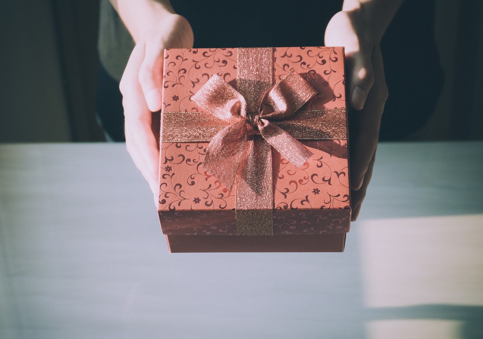 woman's hands holding red gift box with bow; blog: 7 Gifts for Women Going Through IVF